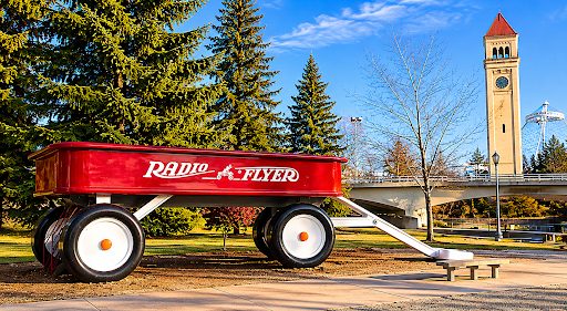 Red Radio Flyer wagon sculpture at Riverfront Park in Spokane, Washington, with the historic Looff Carousel Clock Tower in the background.